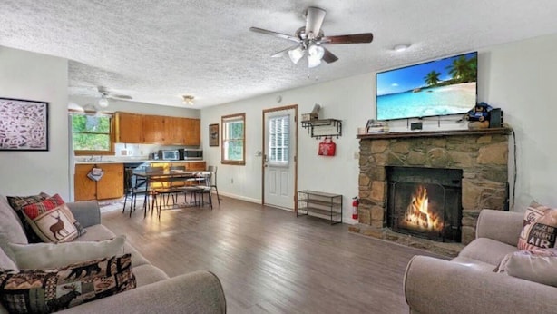A spacious living room with a fireplace, a dining area, and a kitchen in the background.
