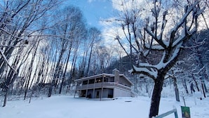 A two-story building with a balcony, surrounded by snow-covered trees and a wooden fence.