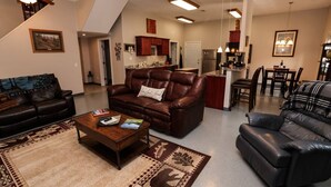 A spacious living room with leather sofas, a coffee table, and a patterned rug. A kitchen and dining area are visible in the background. - Convenient Mountain Comfort (Lincoln)