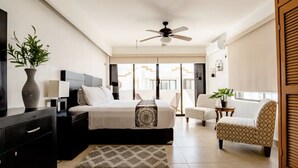 Une chambre à coucher moderne avec un lit, des tables de chevet, un ventilateur de plafond, une chaise, une petite table et une plante en pot.