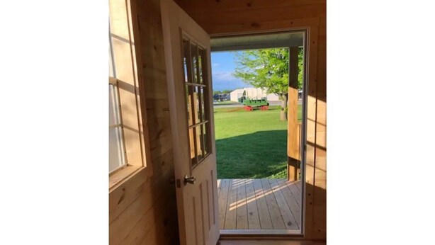 An open wooden door leading to a wooden deck with a grassy yard and a green tractor in the background. - Valley Cabin (Spring Valley)