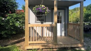 A small wooden structure with a porch, a door, and a hanging flower basket. - Valley Cabin (Spring Valley)