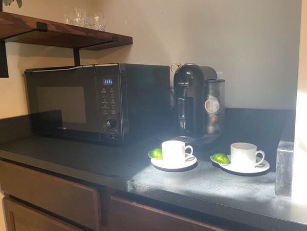 Een keukentafel met een magnetron, een koffiezetapparaat en twee witte kopjes met schotels.