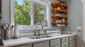 Una cocina con un lavamanos doble, estantes de madera sobre la encimera y una ventana con vista a árboles.