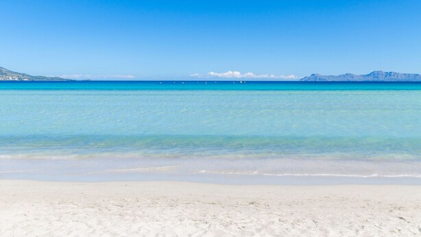 A beach with clear turquoise water and a sandy shore. - YourHouse Mulet, cozy sea-view apartment (Can Picafort)