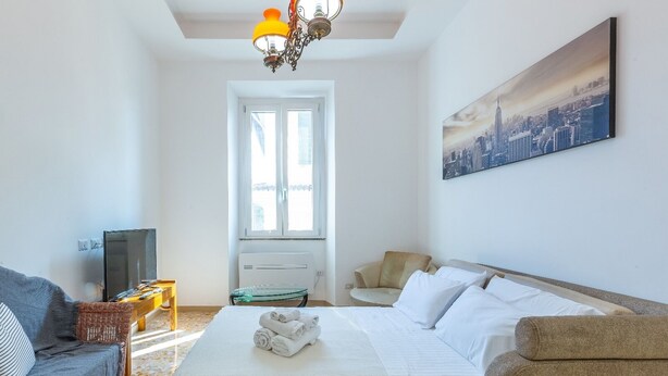 Quarto de hotel com cama, sofá, televisão, janela e pintura de paisagem urbana.