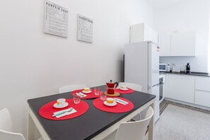 A modern kitchen with white cabinets and a black countertop. There is a dining table with red placemats and white chairs.