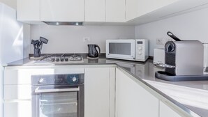 Cozinha moderna com armários brancos, fogão a gás, micro-ondas e máquina de café.