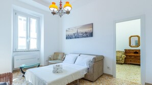 Um quarto com cama, uma cadeira, cômoda e uma pintura da paisagem urbana.