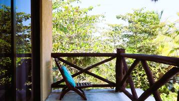 Un balcon doté d’une balustrade en bois, d’un banc et offrant une vue sur une végétation luxuriante.