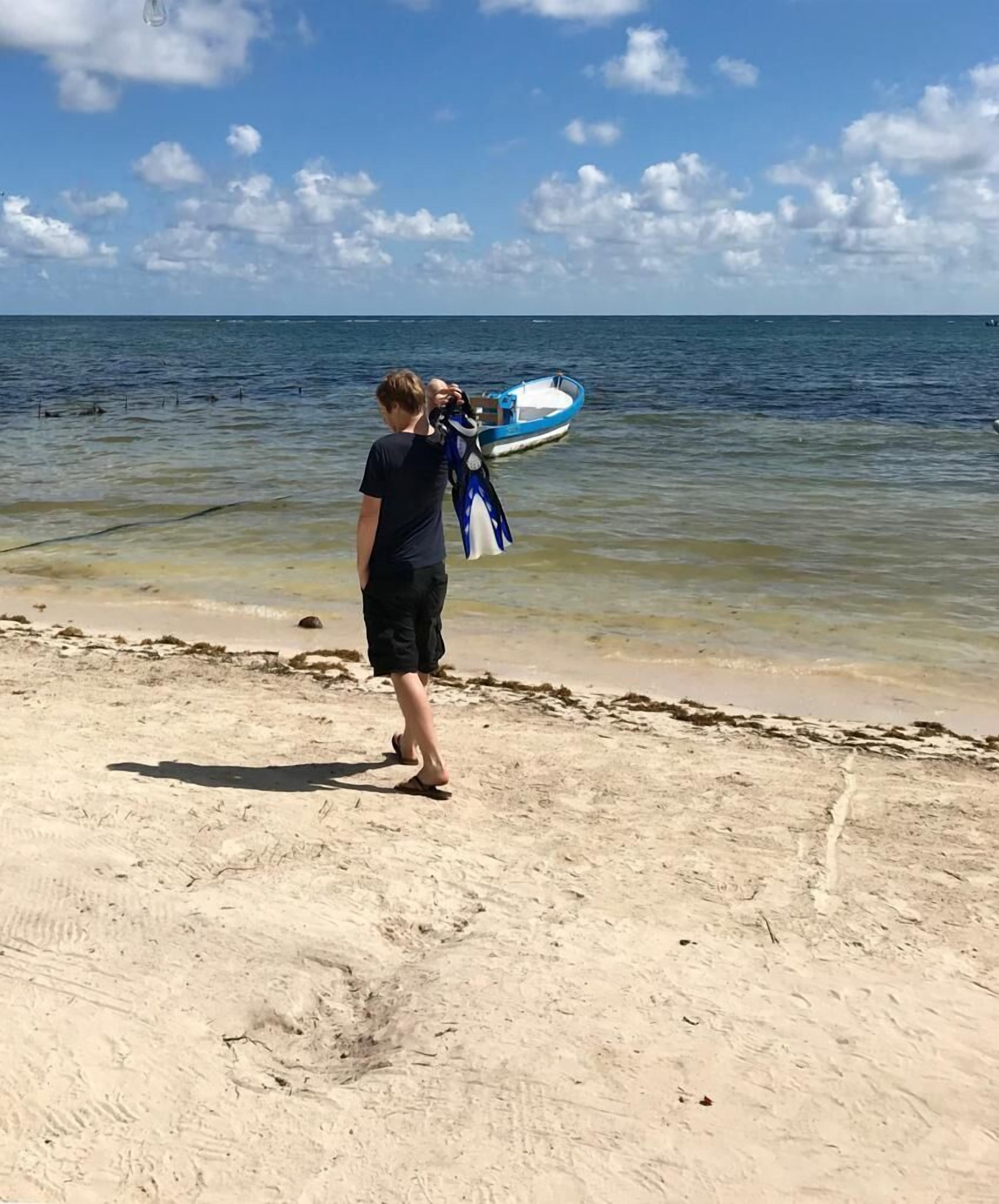 Una persona está de pie en una playa arenosa sosteniendo una tabla de surf azul y blanca.