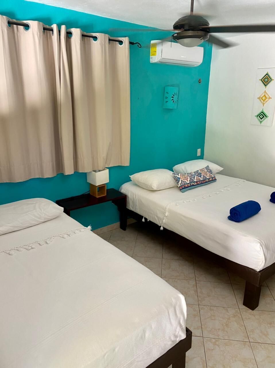 A room with two beds, a ceiling fan, an air conditioning unit, and a wall-mounted light switch.