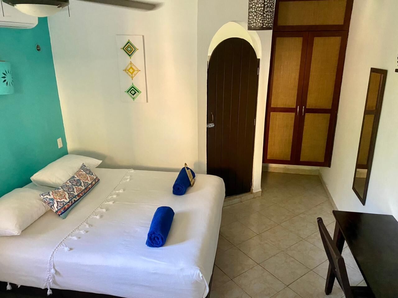 A hotel room with a bed, a desk, a wardrobe, and a door leading to another room.