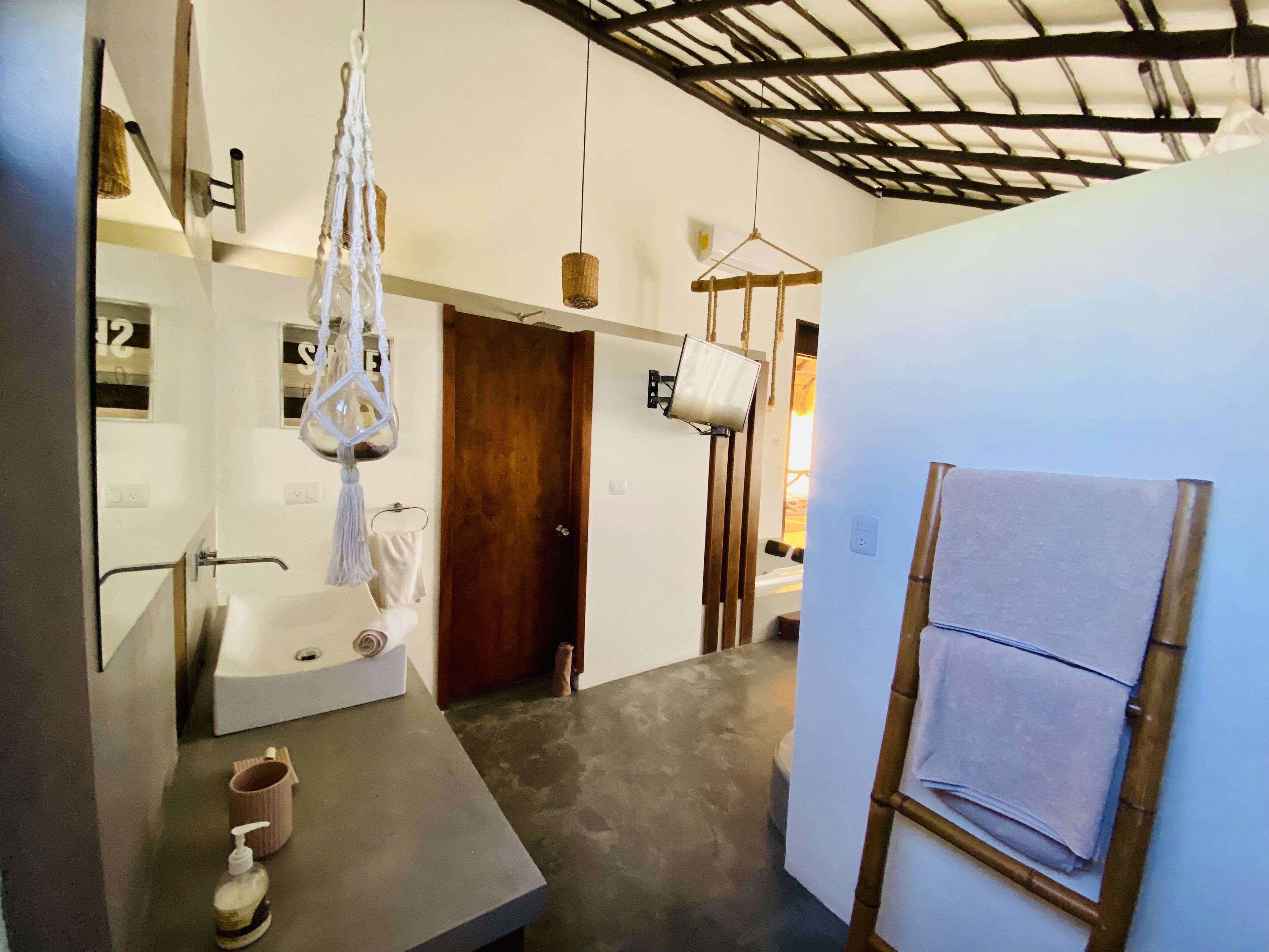 A bathroom with a bathtub, a sink, a toilet, and a shower area. There is a wooden door and a towel rack.