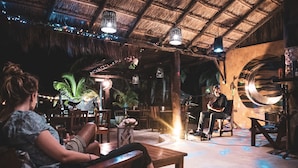 A rustic interior with wooden furniture, a thatched roof, and string lights. - Hotel Luna de Plata (Mahahual)