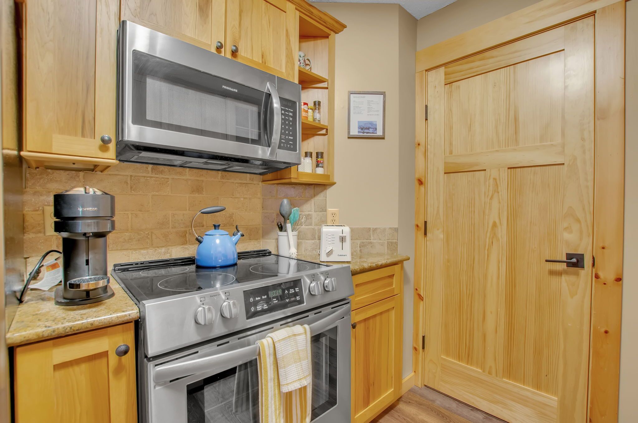Una cocina con armarios de madera, microondas de acero inoxidable, estufa a gas y cafetera.