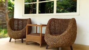 A room with two wicker chairs and a small table, a window with a view of greenery, and a tiled floor. - Tengger Guest House (Pasuruan)