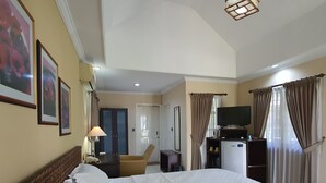 A hotel room with a large bed, a desk, a chair, a television, and a minibar. - Tengger Guest House (Pasuruan)