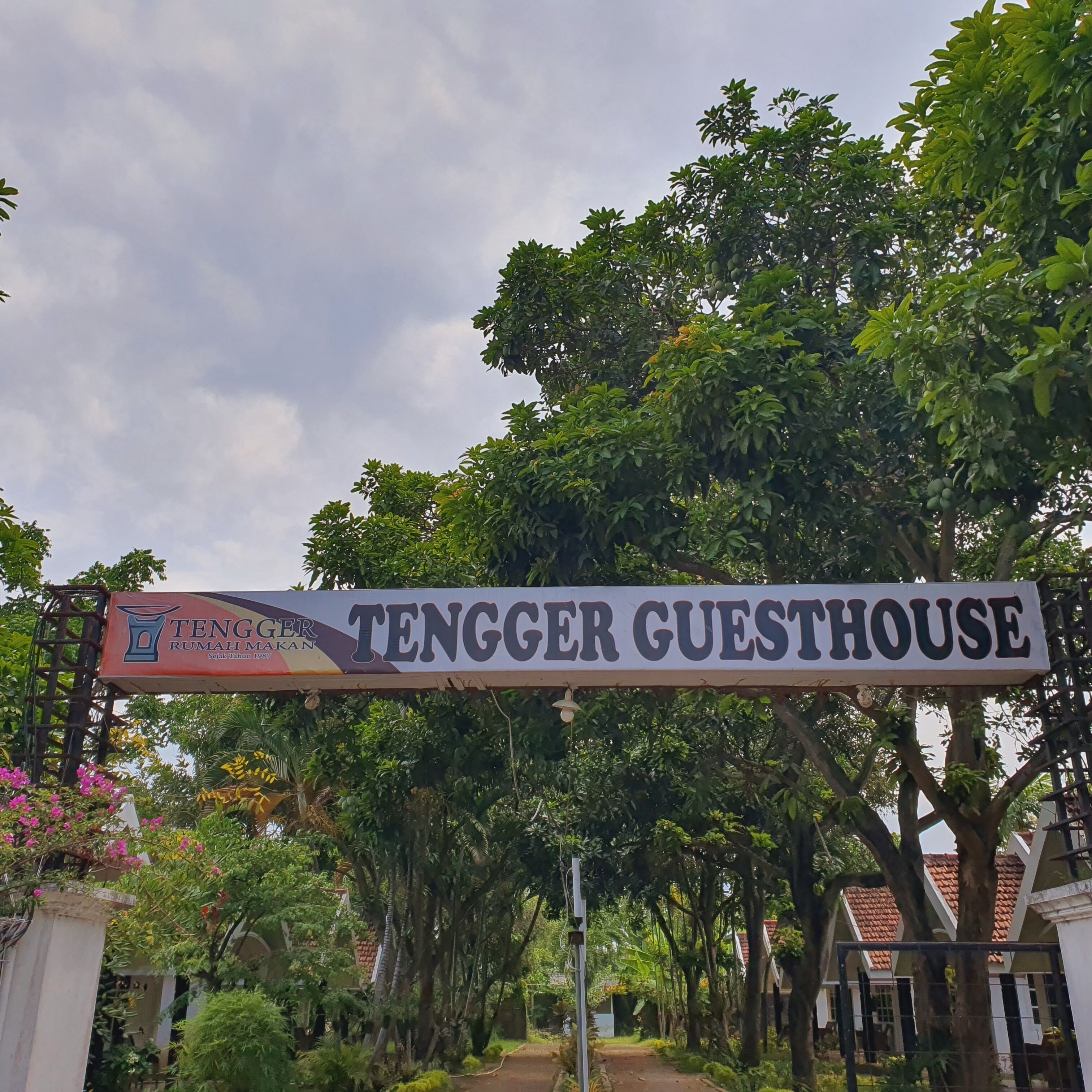 A sign for 'TENGGER GUESTHOUSE' with a logo and text indicating it is a property of 'TENGGER RUMAH Makan' established in 1987.