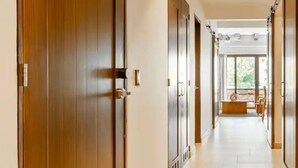 Un pasillo con puertas de madera, suelo de baldosas y vistas a un balcón con mobiliario exterior.