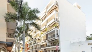 Un edificio residencial de varios pisos con balcones, coches aparcados y palmeras.