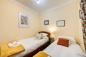 A hotel room with two single beds, a nightstand with a lamp, and a framed picture on the wall.