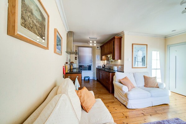 A spacious living room with a sofa and a dining area with wooden cabinets and a kitchen in the background.