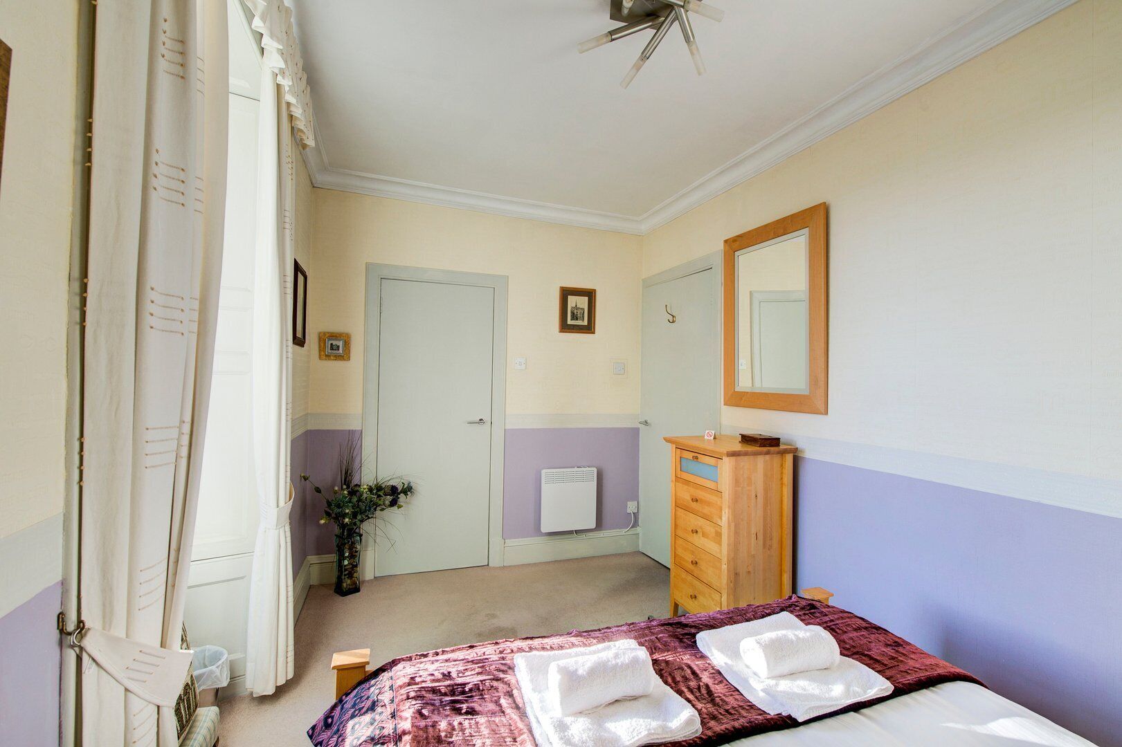 Una camera da letto con un letto, una cassettiera, uno specchio e un termosifone.