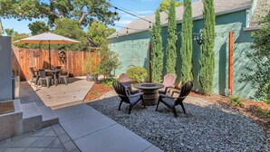 A patio area with a round table and chairs, a wooden fence, and tall trees.
