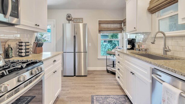 A modern kitchen with stainless steel appliances, white cabinetry, and a granite countertop.