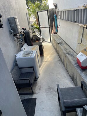 A narrow outdoor space with a washing machine, a utility sink, and a metal railing.
