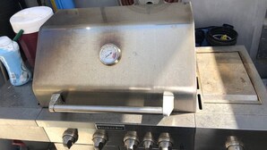 Un barbecue en acier inoxydable doté d’un manomètre, d’un tuyau et d’une cheminée de ventilation.