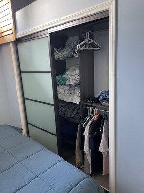A bedroom with a bed, a wardrobe with clothes, and a hanging rack.