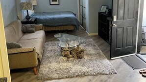 Un espace de vie compact comprenant un lit, un canapé et une table basse avec un plateau en bois naturel.