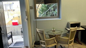 Un coin repas avec une table en verre et des chaises en osier, une fenêtre avec des stores et un four à micro-ondes posé sur un comptoir.