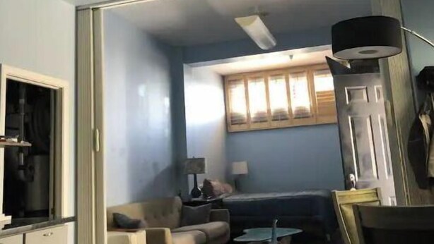 Un salon avec un canapé, une table basse et une lampe. Une porte donne accès à une autre pièce.