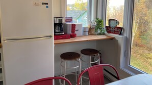 Una cocina con refrigerador, cafetera y ventana con vista a árboles.