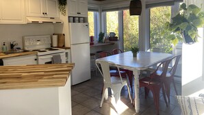 Una cocina con armarios blancos, encimera de madera, estufa, refrigerador y una mesa de comedor con sillas.