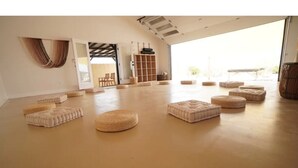 A spacious room with a high ceiling, a large open door leading outside, and several round and square ottomans arranged on the floor. - Mystic Sky Ranch 5 Bedrooms with Yoga Studio & Spa (Landers)