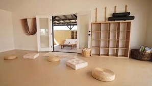 A room with a large open space, a wooden shelf unit, and a view through an open door to an outdoor area with a chair and a table. - Mystic Sky Ranch 5 Bedrooms with Yoga Studio & Spa (Landers)