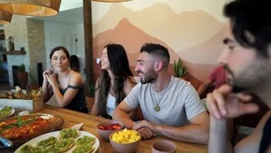A group of people seated at a table with various dishes, including pizza and fruit, in a room with a mountain mural on the wall. - Mystic Sky Ranch 5 Bedrooms with Yoga Studio & Spa (Landers)
