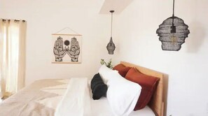 A bedroom with a bed, a hanging light, and a wall art piece.