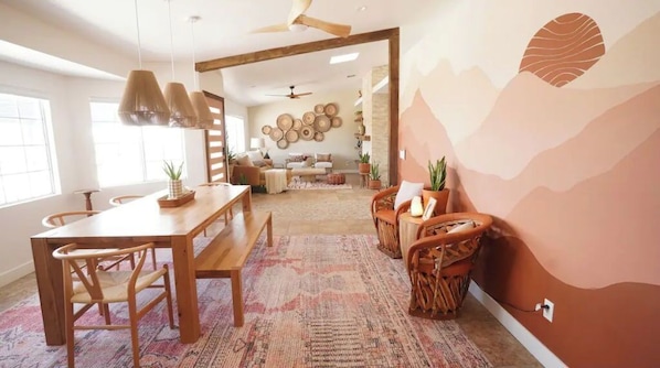 A spacious living area with a wooden dining table, chairs, and a patterned rug.