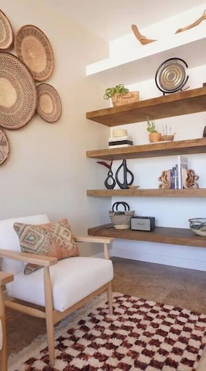 A living room with a wooden chair, a patterned rug, and a wall decorated with woven baskets and a metal sculpture.