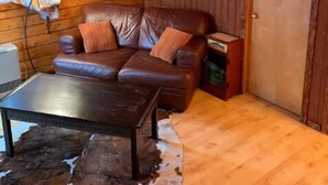 Un intérieur de chalet chaleureux avec un canapé en cuir, une table en métal et un tapis en peau de vache.