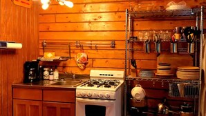 Une cuisine avec des murs en bois, une cuisinière à gaz, un évier et des étagères remplies de vaisselle et d’ustensiles de cuisine.