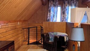 Une pièce mansardée chaleureuse avec des murs en bois, un plafond en pente, un lit, un bureau, une chaise, une lampe et une fenêtre avec des rideaux.