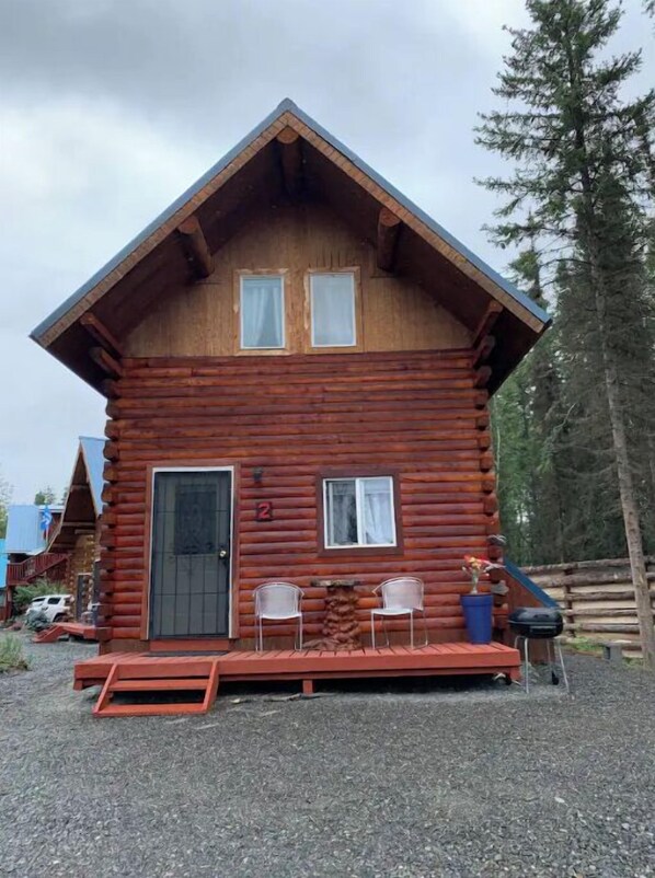 A log cabin with a front porch, two windows, and a door.