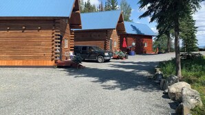 Une cabane en rondins avec une allée en gravier et un VUS garé devant.