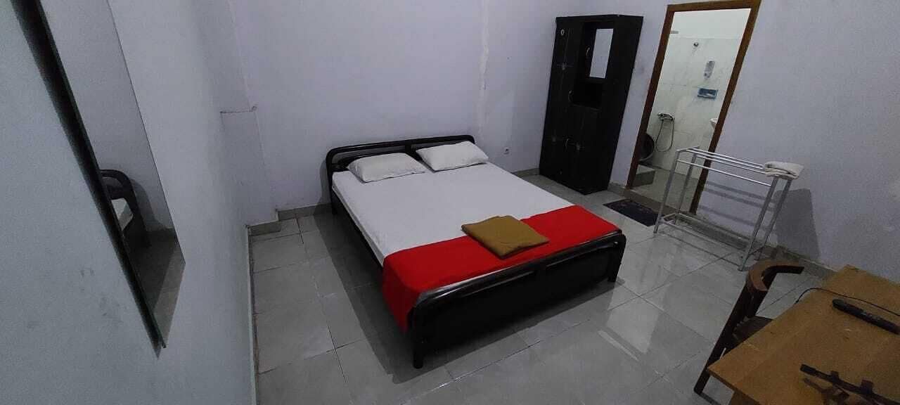 A small, clean room with a single bed, a wooden nightstand, a mirror, and a door.